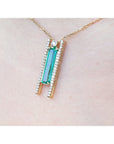 A close-up of a 14K yellow gold necklace with a baguette-cut emerald and natural diamond accents worn on a person's neck.