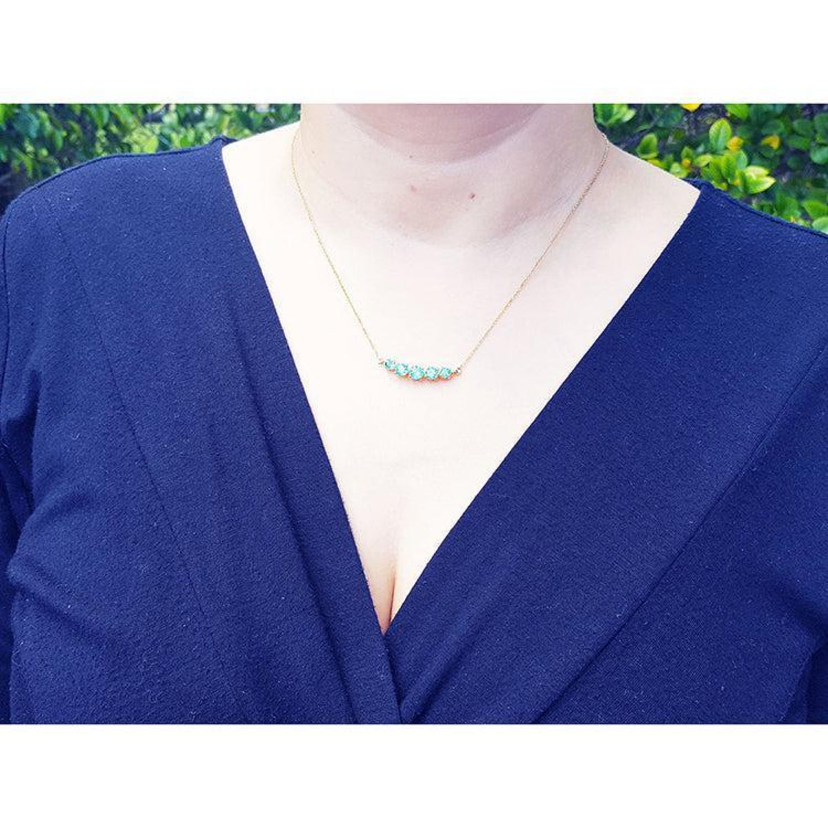 14K gold necklace with five round, medium light green Colombian emeralds of varying sizes.