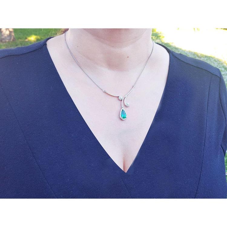 Woman wearing a blue dress with a white gold necklace featuring a natural emerald pendant in a halo diamond