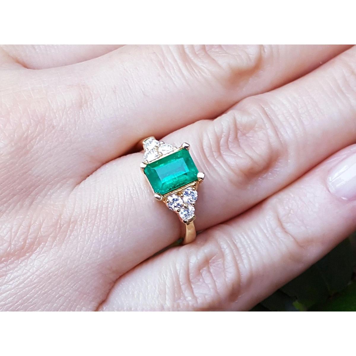 A yellow gold ring with a natural emerald and diamond accents on a finger.