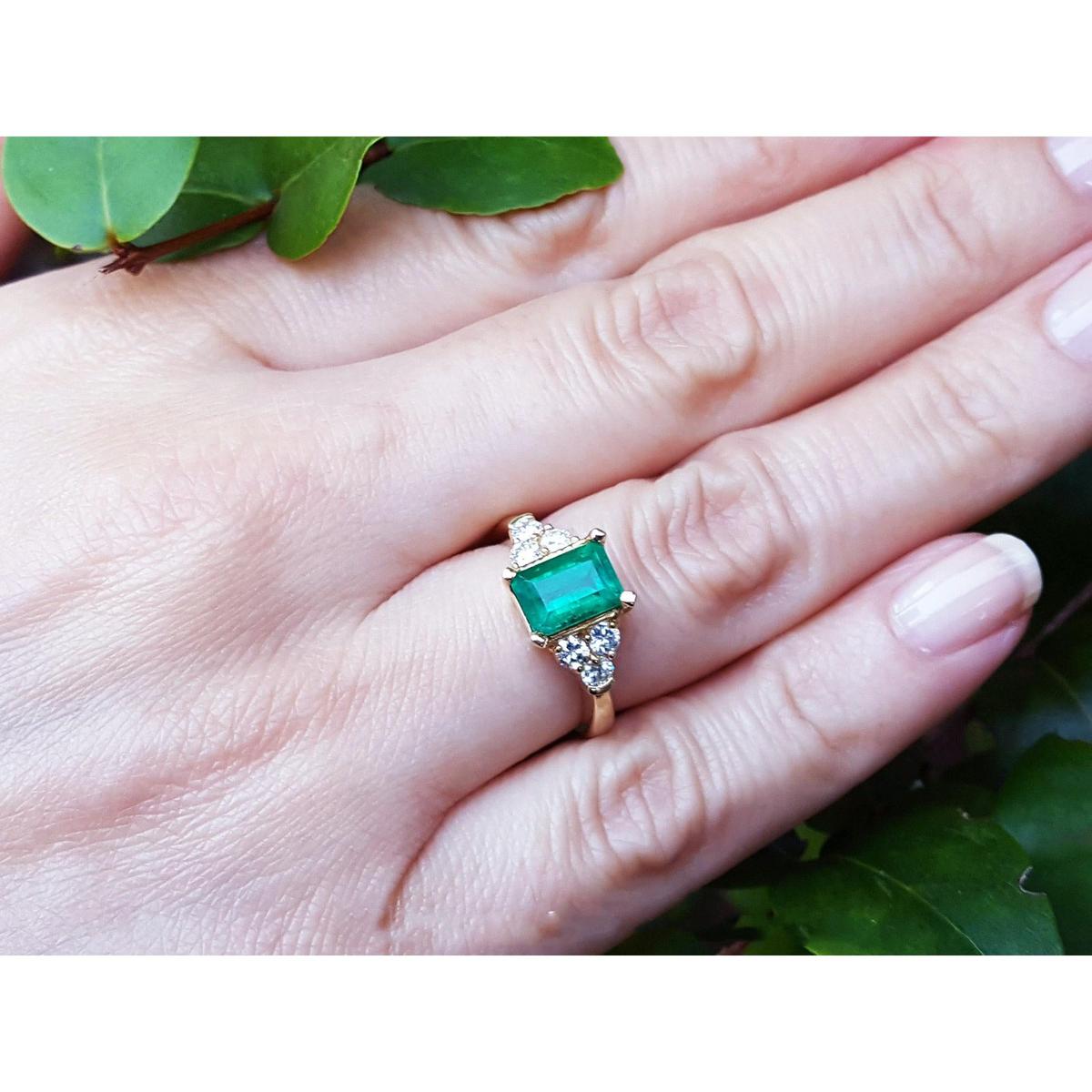 Gold ring with an emerald and diamond accents on a leafy background.
