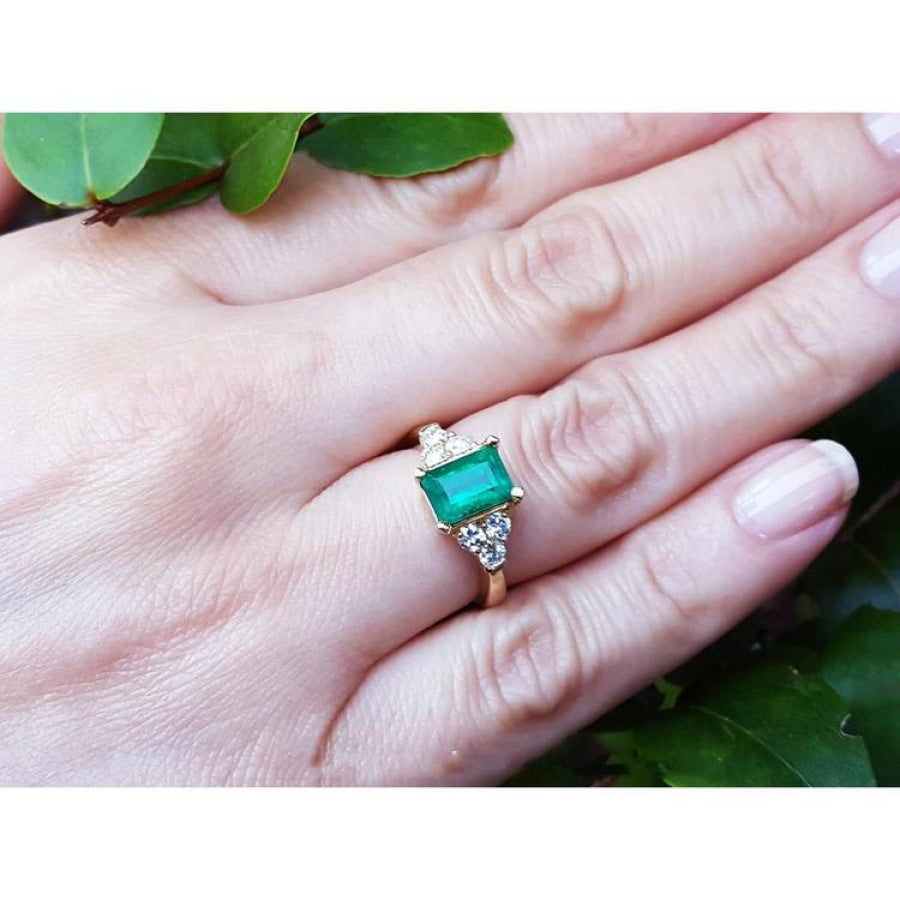 Women's 14K yellow gold ring with a rectangular emerald and three accent diamonds on each side.