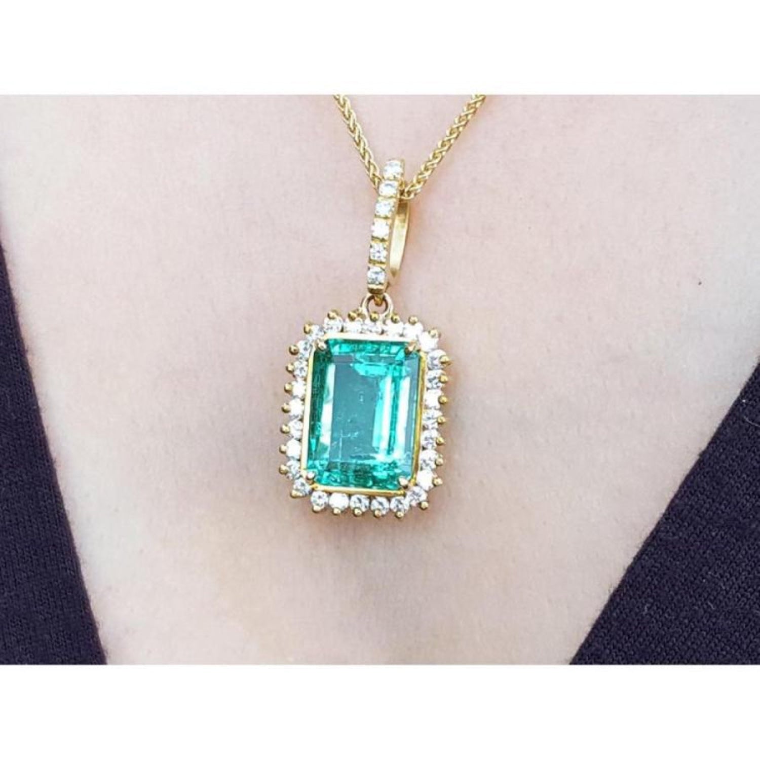 Emerald-cut emerald pendant with halo diamonds in 18K gold, worn on a necklace.