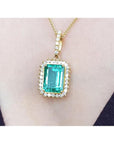 Emerald-cut emerald pendant with halo diamonds in 18K gold, worn on a necklace.