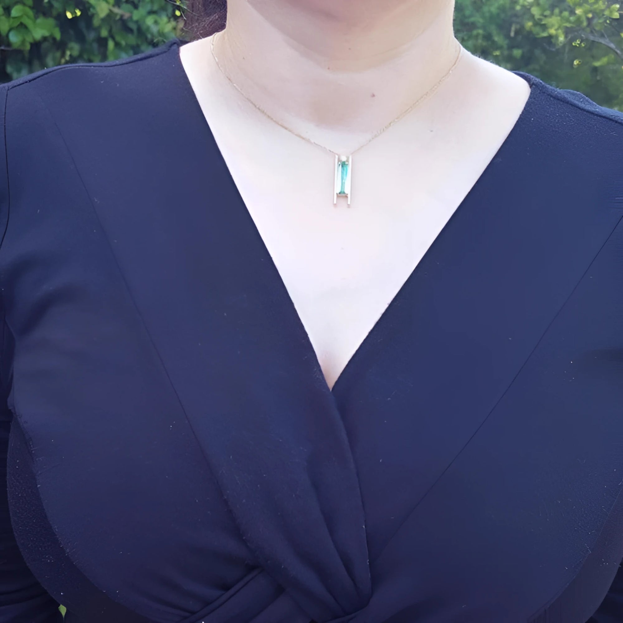 Emerald baguette cut necklace with natural diamonds, 14K yellow gold, worn on a black top.
