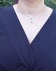 Navy blue top worn by a woman with a baguette cut emerald necklace featuring a rectangular pendant.