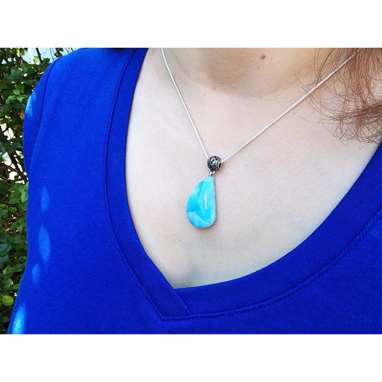 Person wearing a blue teardrop pendant necklace with a blurred green background