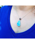 Person wearing a blue teardrop pendant necklace with a blurred green background