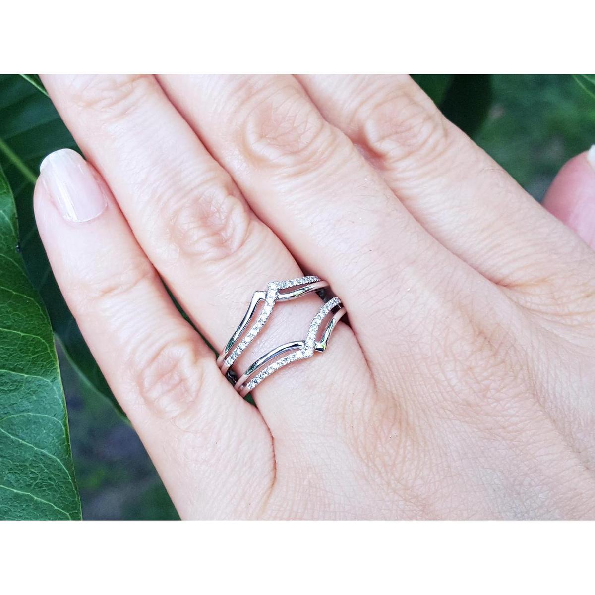 Hand wearing a wrap enhancer for solitaire rings on a blurred green background.