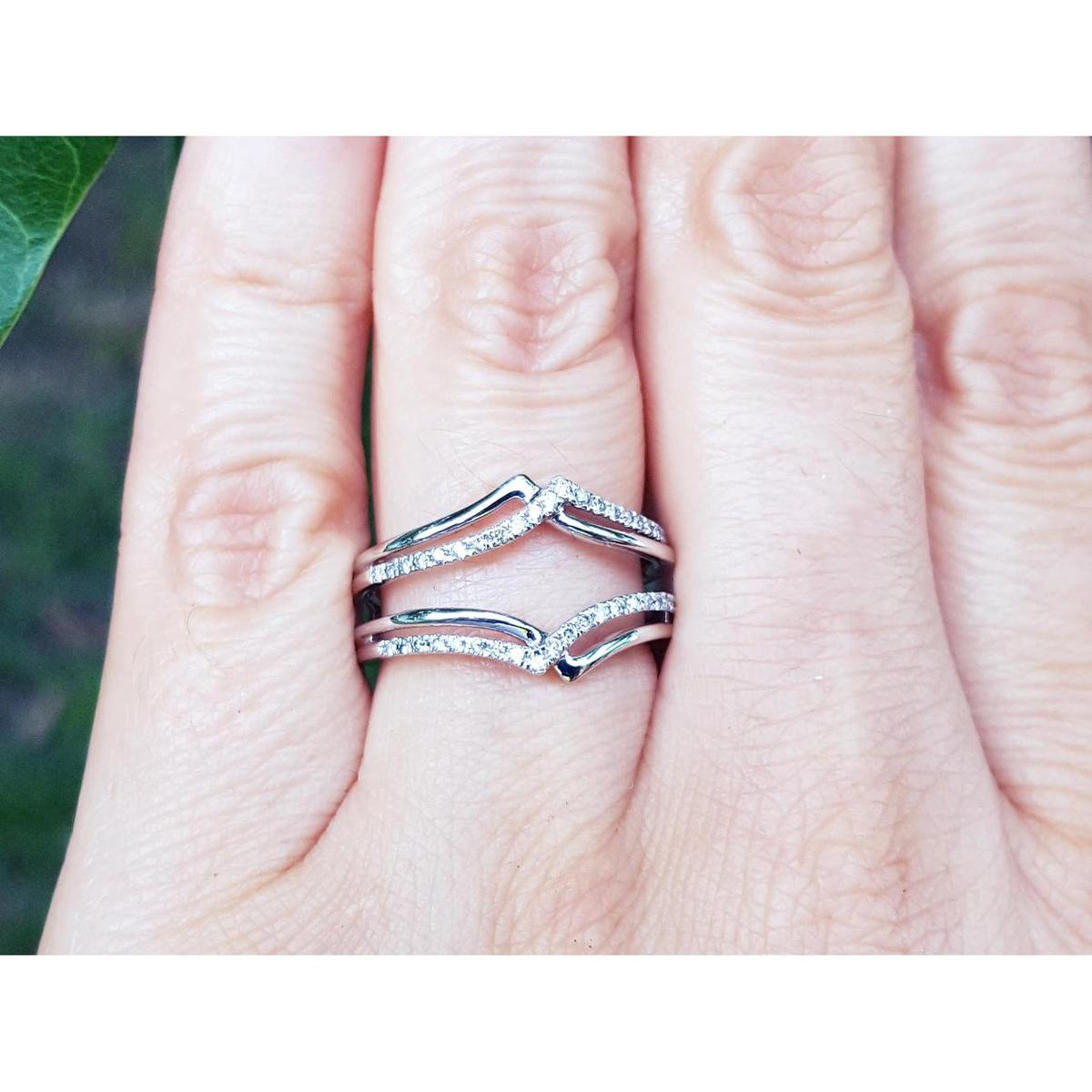 Close-up of a hand wearing a diamond ring guard enhancer wrapper 14k white gold with a blurred green background.