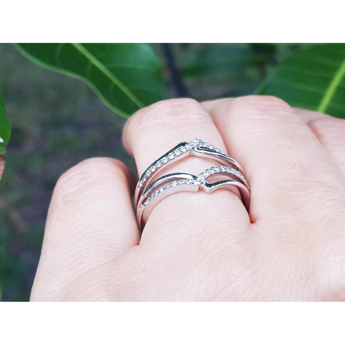 White gold wrapper natural diamonds enhancer ring on a finger with a blurred green leafy background.