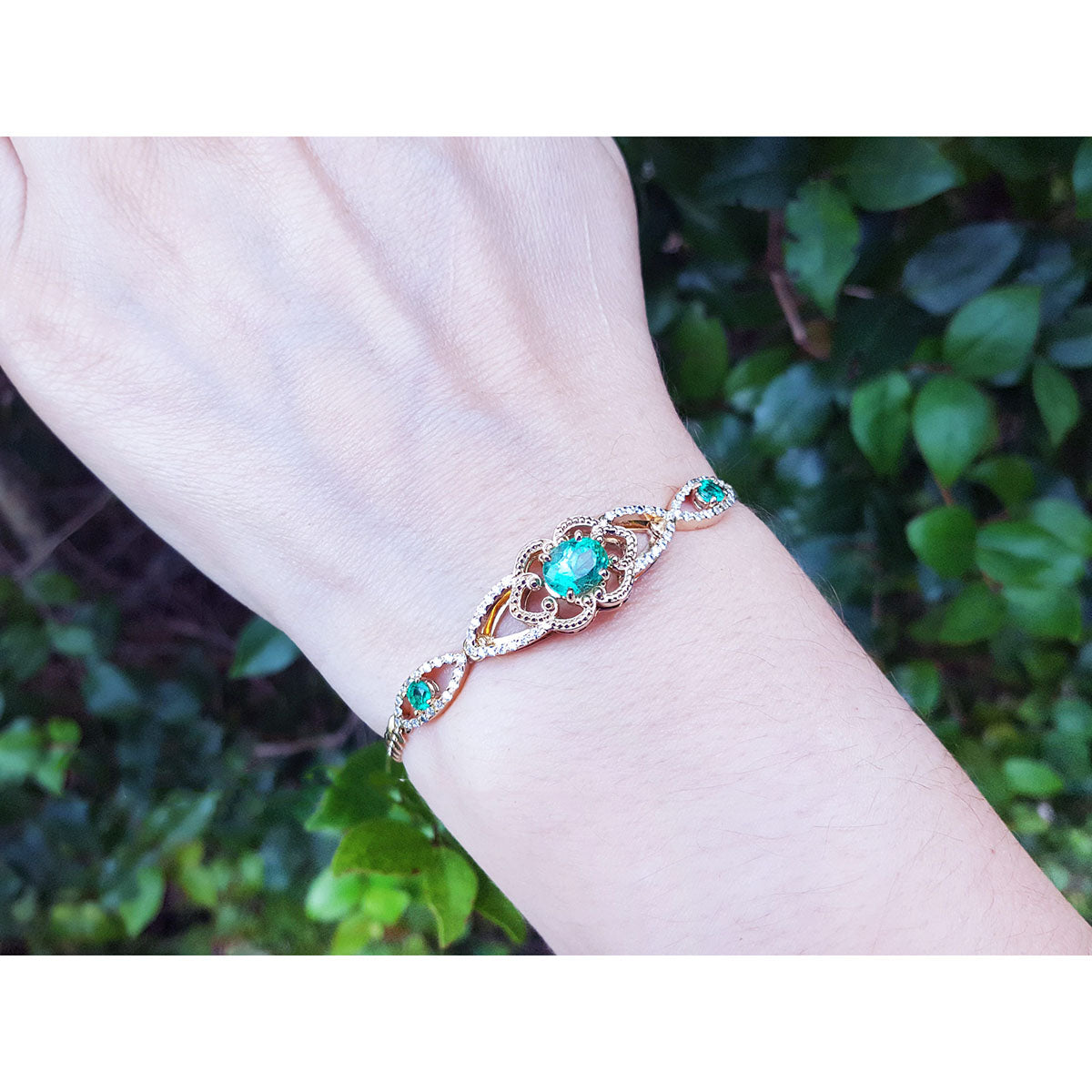 Bracelet with oval emerald on a wrist against a blurred green leafy background.