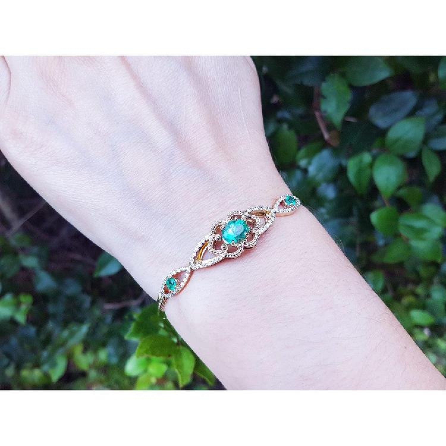 Emerald oval cut bracelet in 14K yellow gold with diamonds, worn on a wrist.