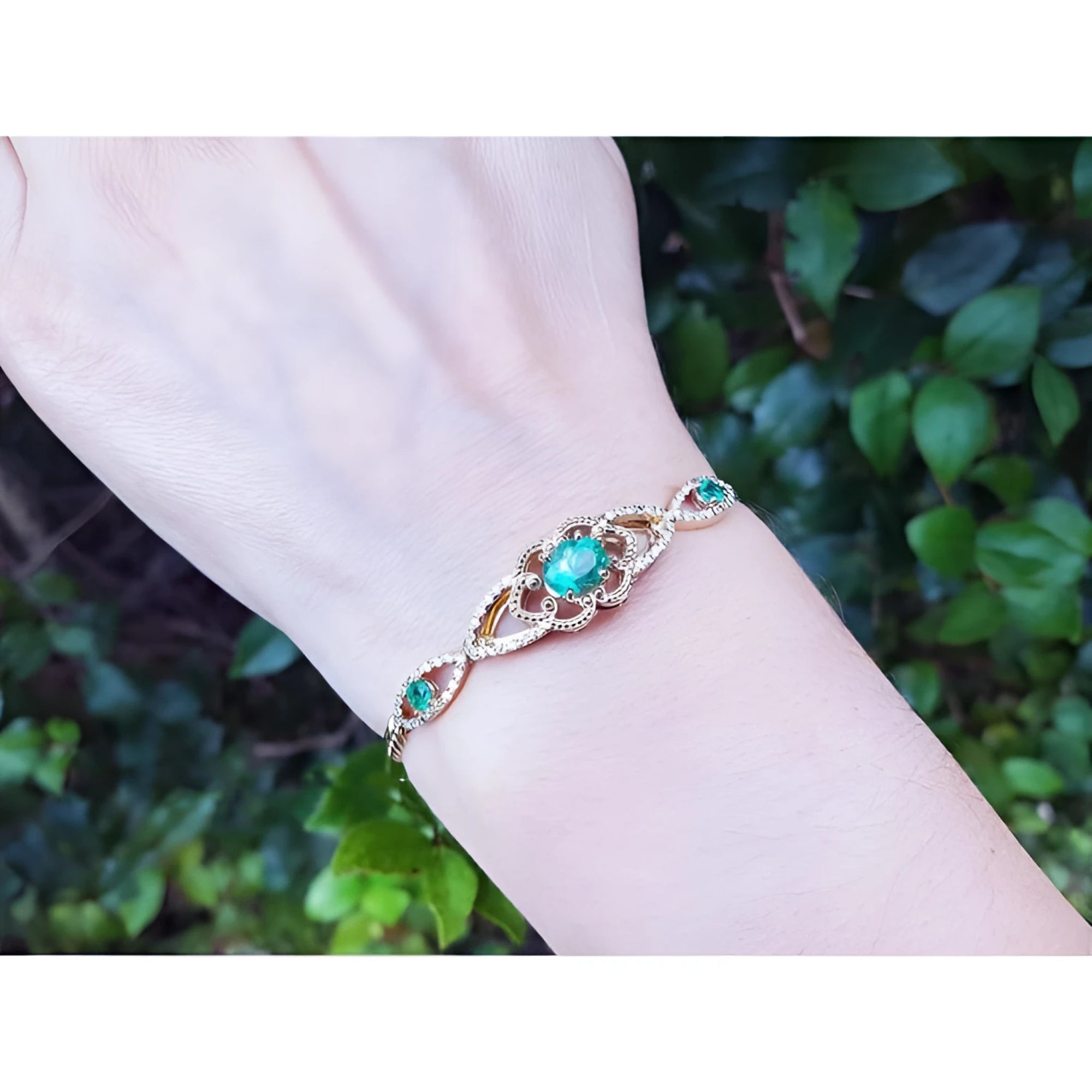 Emerald oval cut bracelet in 14K yellow gold with diamonds, worn on a wrist.