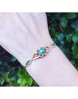 Bracelet with oval emerald on a wrist against a blurred green leafy background.