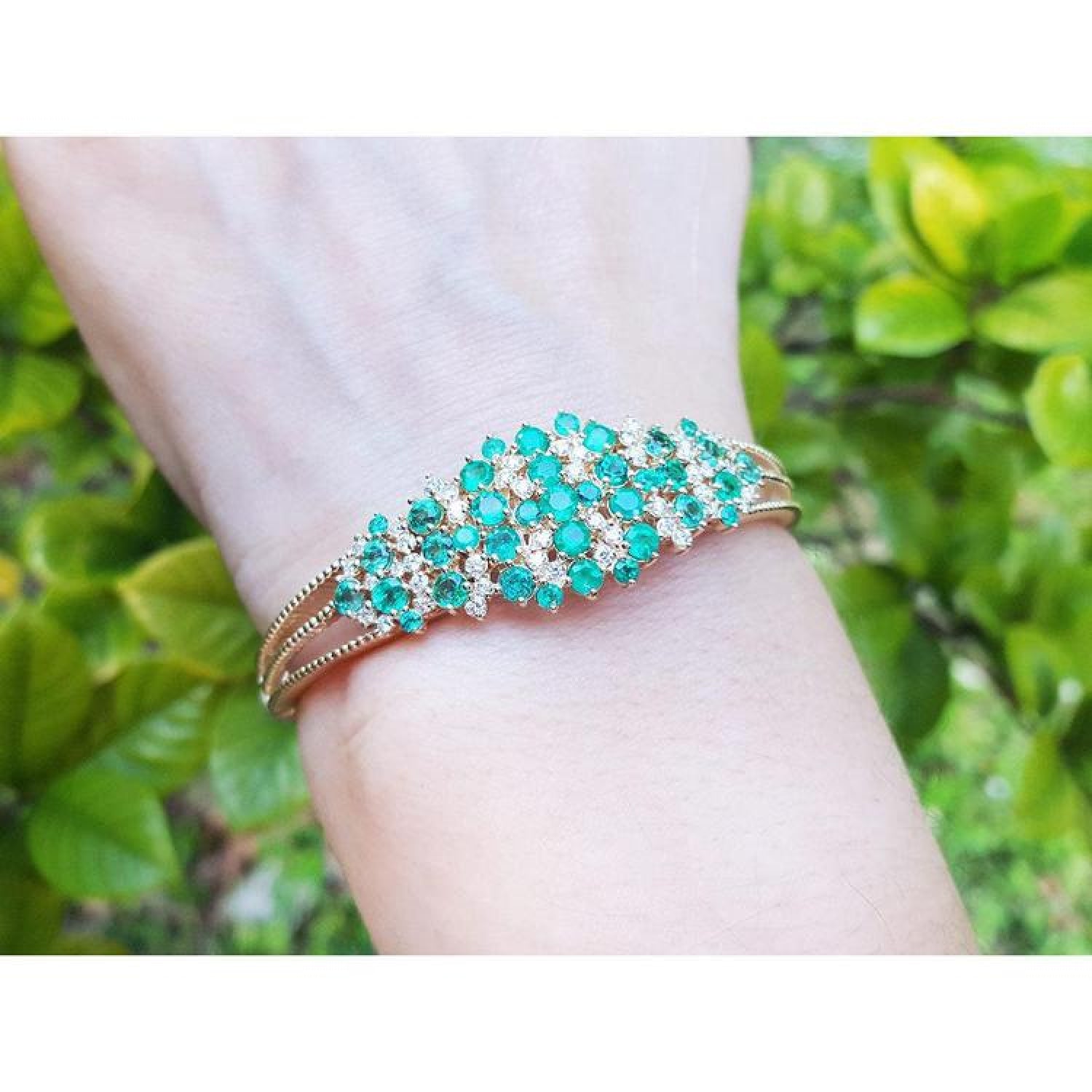 14K yellow gold bangle with round Colombian emeralds and diamonds in a floral design.