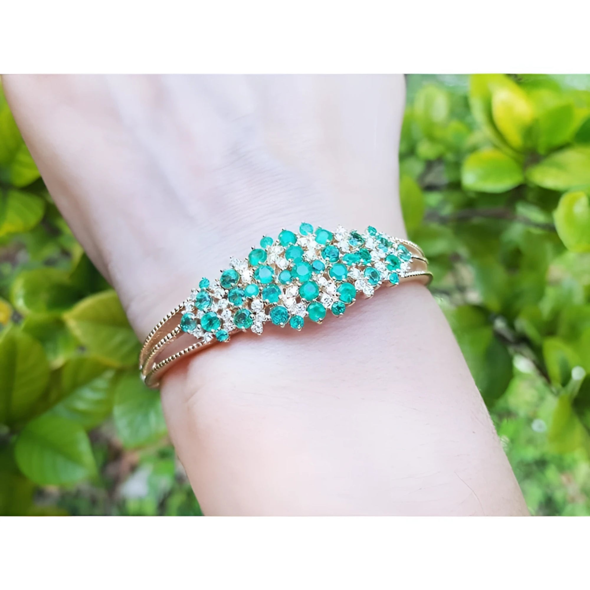 14K yellow gold bangle with round Colombian emeralds and diamonds in a floral design.