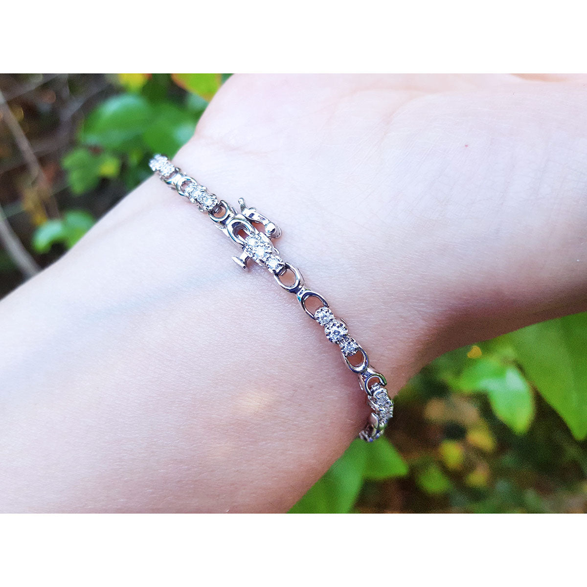 White gold bracelet with diamonds on a wrist with a blurred green background.