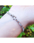White gold bracelet with diamonds on a wrist with a blurred green background.