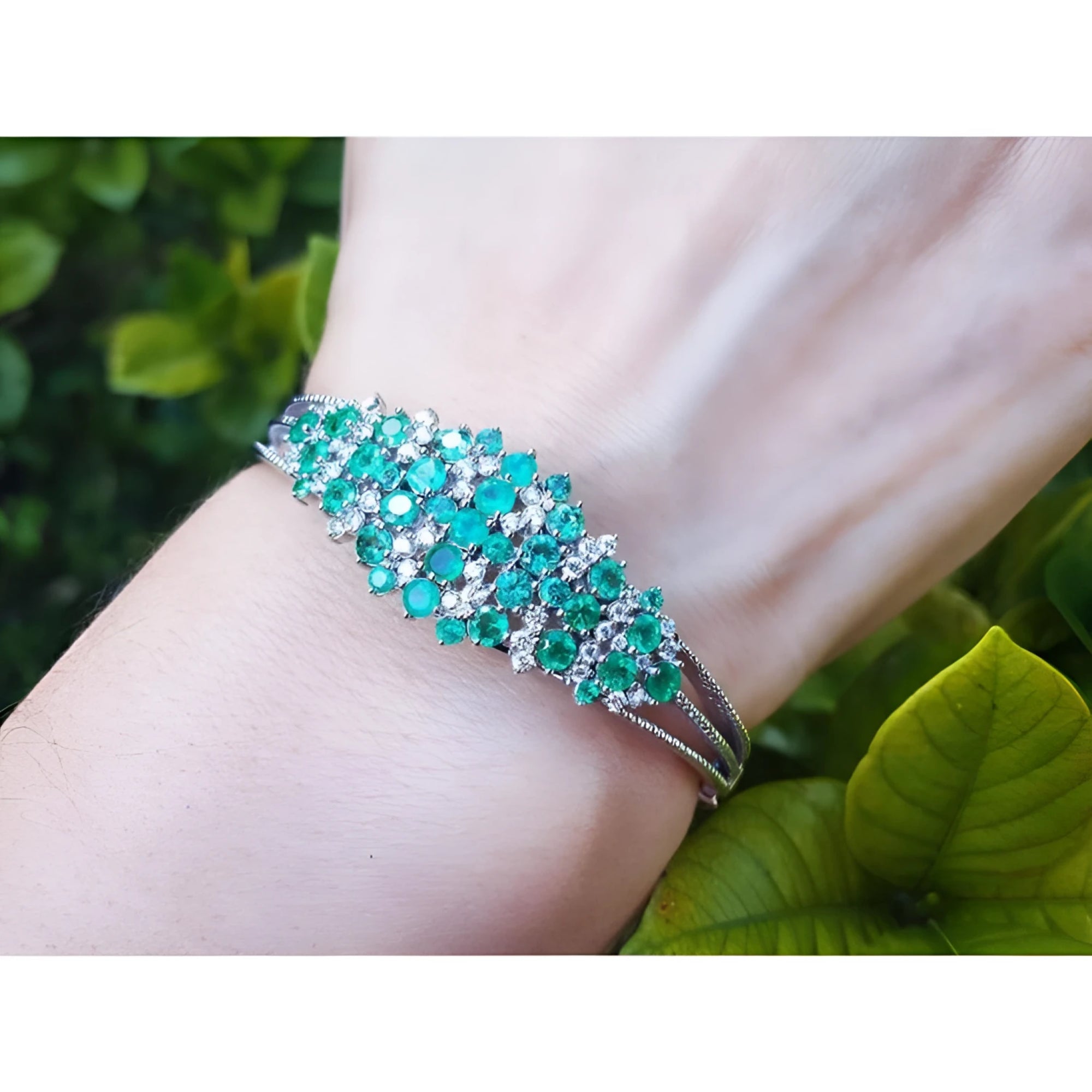 14k white gold bangle bracelet with round Colombian emeralds and diamonds on a wrist.