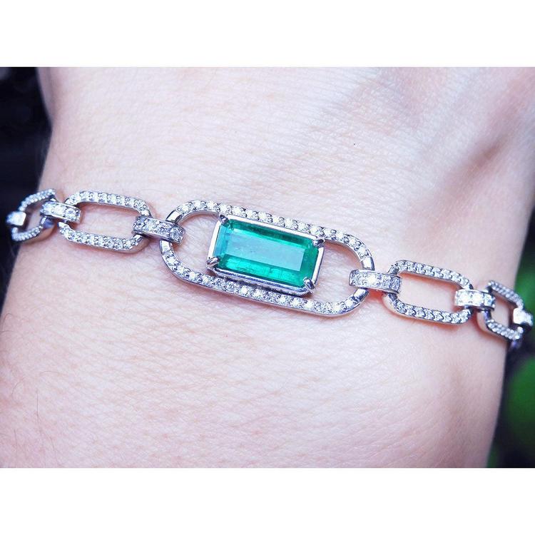 White and yellow gold paperclip bracelet with an emerald-cut natural emerald on a wrist against a neutral background.