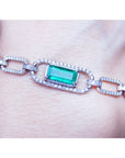 White and yellow gold paperclip bracelet with an emerald-cut natural emerald on a wrist against a neutral background.