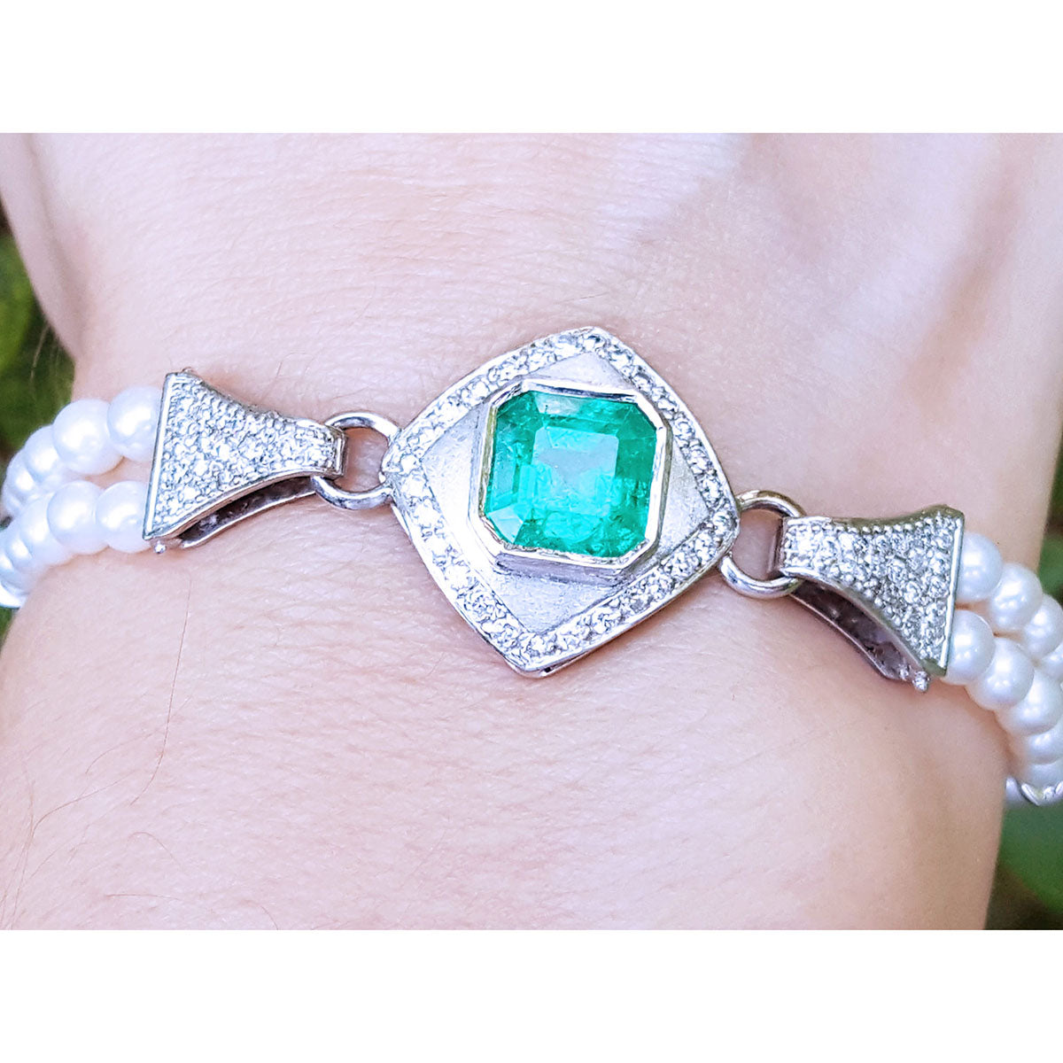 Emerald-cut Colombian emerald and pearls bracelet crafted in 18k white gold on a wrist.