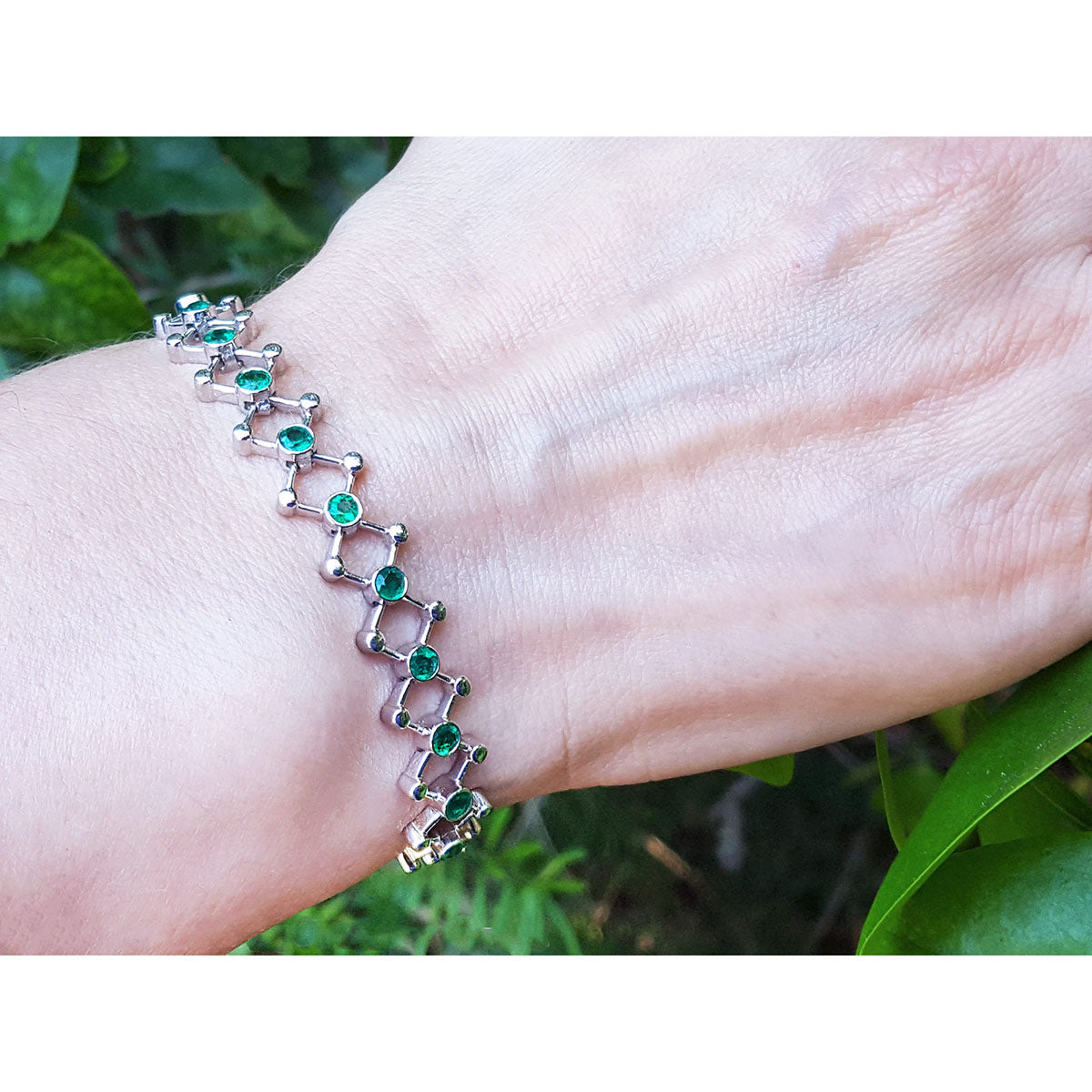 Bracelet with round cut emeralds on a wrist against a natural background.