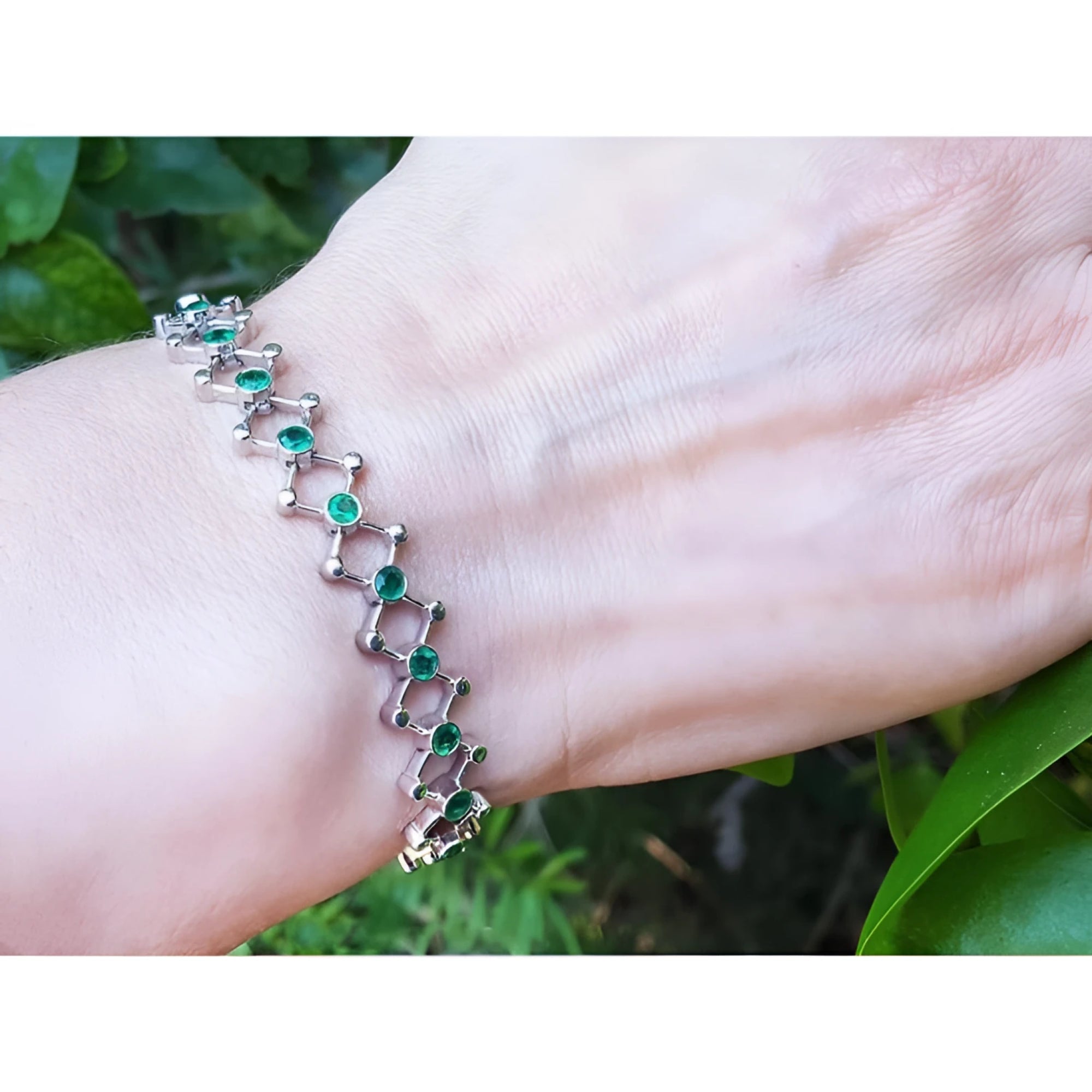 14K white gold bracelet with round Colombian emeralds in bezel-set diamond-shaped links on a wrist.