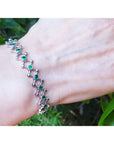 Bracelet with round cut emeralds on a wrist against a natural background.