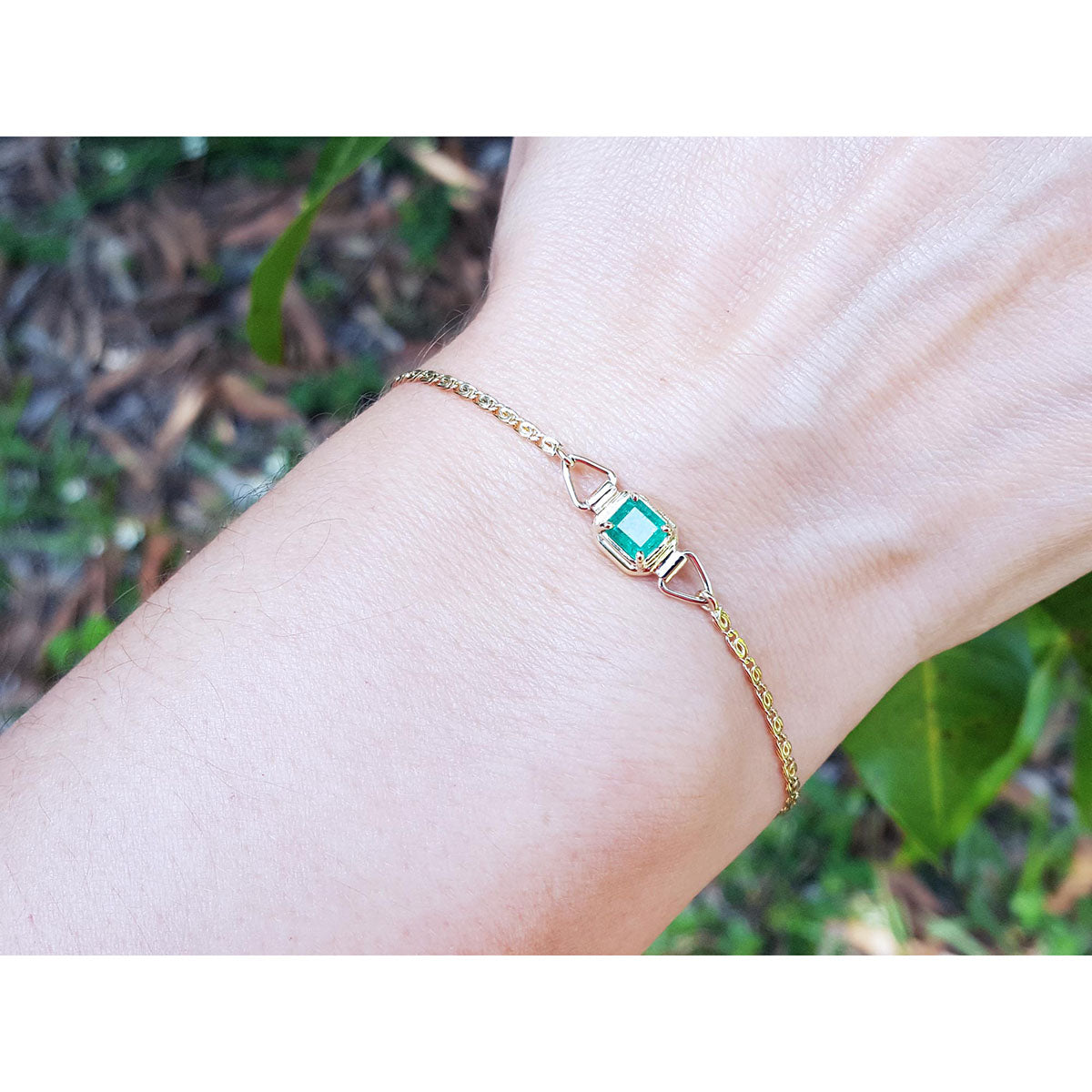 On women&#39;s wrist natural emerald solitaire bracelet crafted in 14k yellow gold against a natural background.