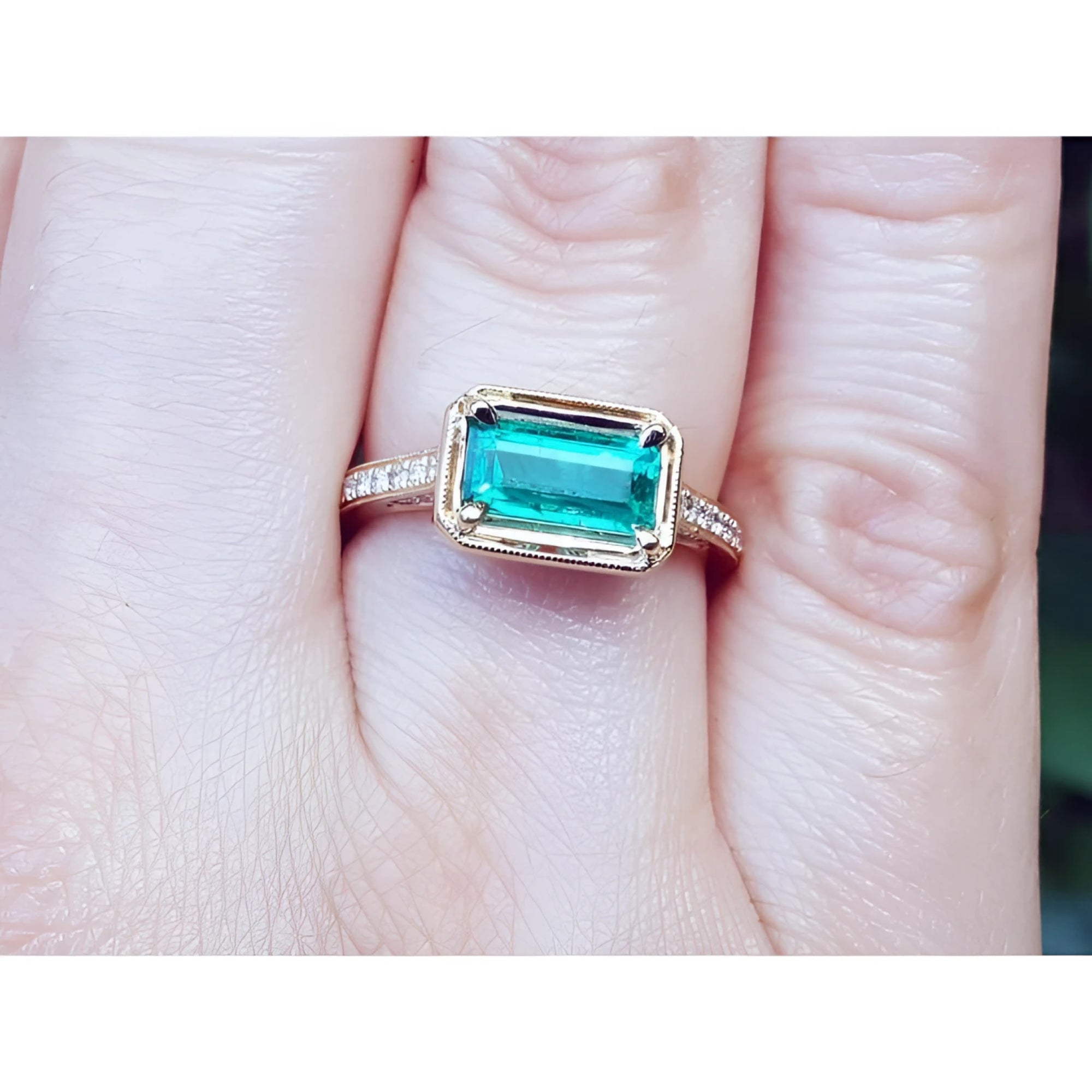 Hand wearing a natural emerald ring east west orientation prong set in yellow gold.