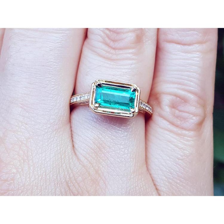 Hand wearing a natural emerald ring east west orientation prong set in yellow gold.
