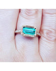 Hand wearing a natural emerald ring east west orientation prong set in yellow gold.