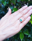 A hand's person wearing a natural colombian emerald ring on a green leafy background.