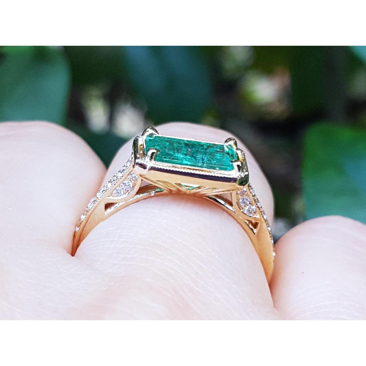 The underside view of a colombian emerald ring in yellow gold on a finger.