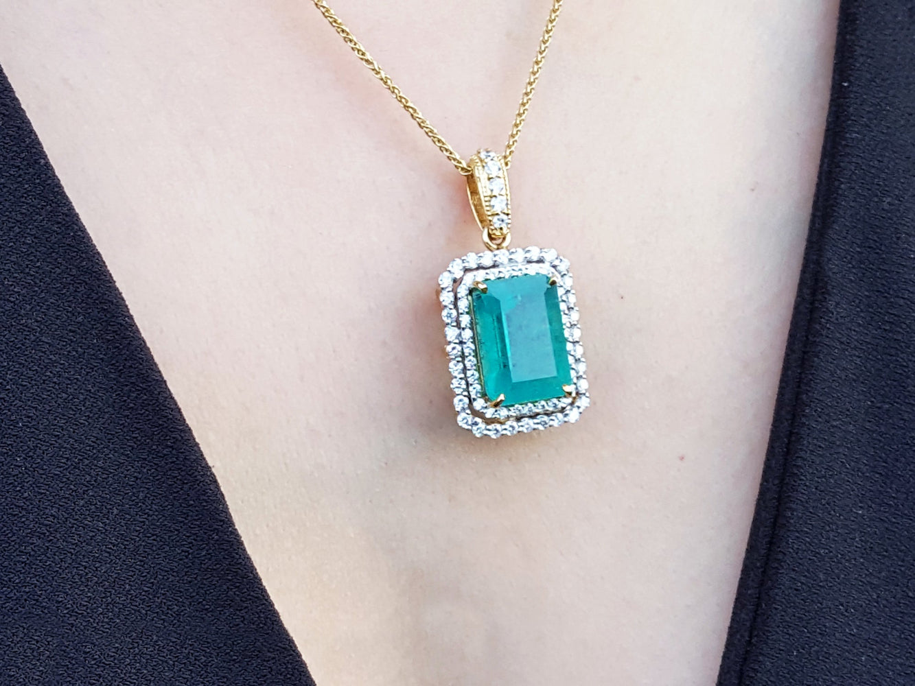 Gold necklace with a natural emerald pendant on a person wearing a black outfit.