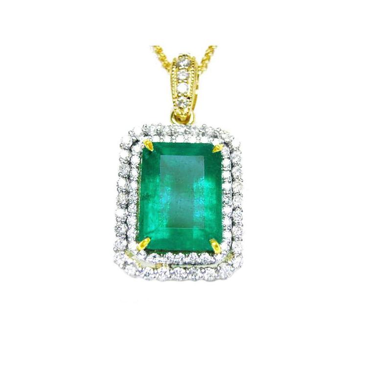 The topside of a pendant with a rectangular emerald encircled by a double halo diamond in yellow gold.