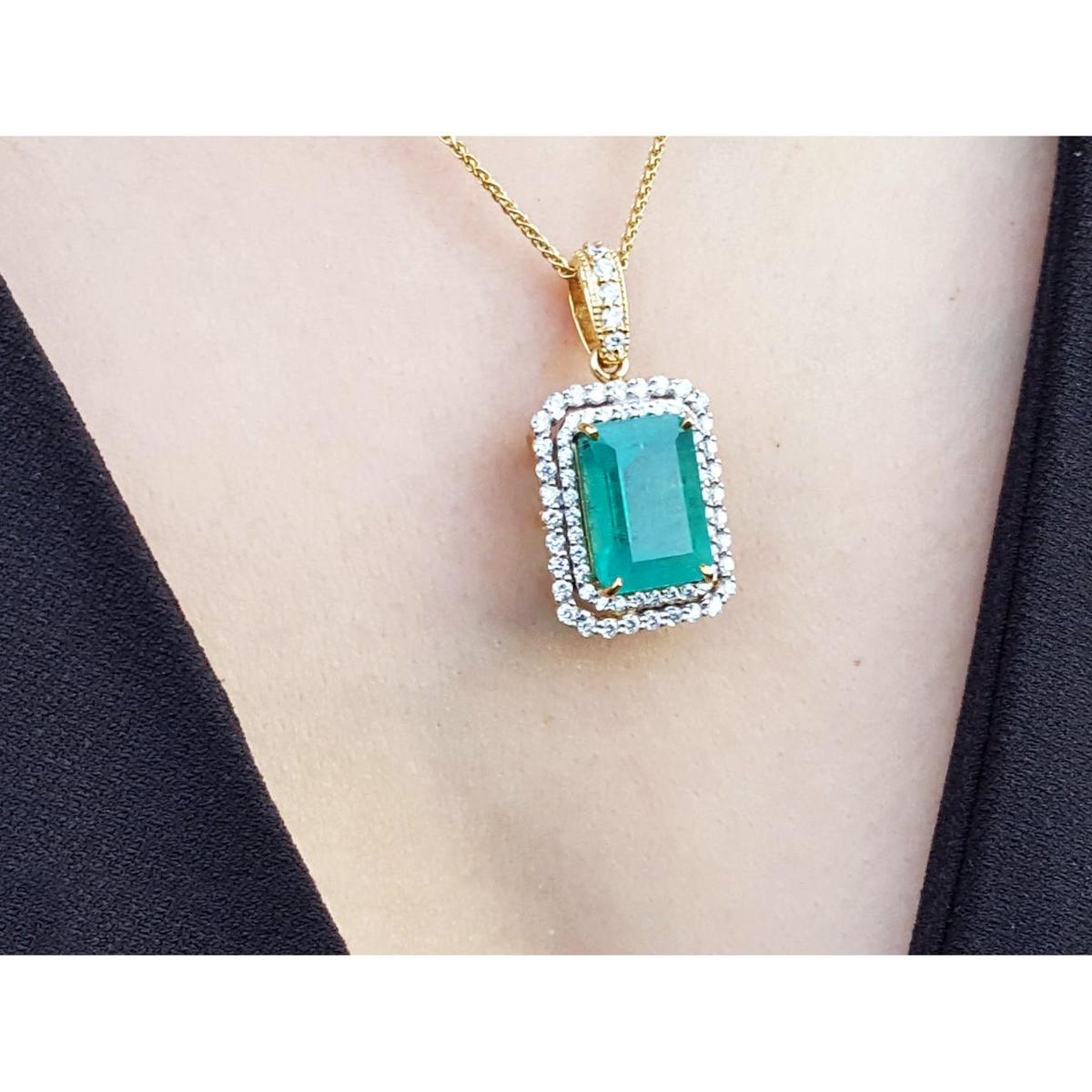 Gold necklace with a natural emerald into a double halo diamond pendant on a person's neck.