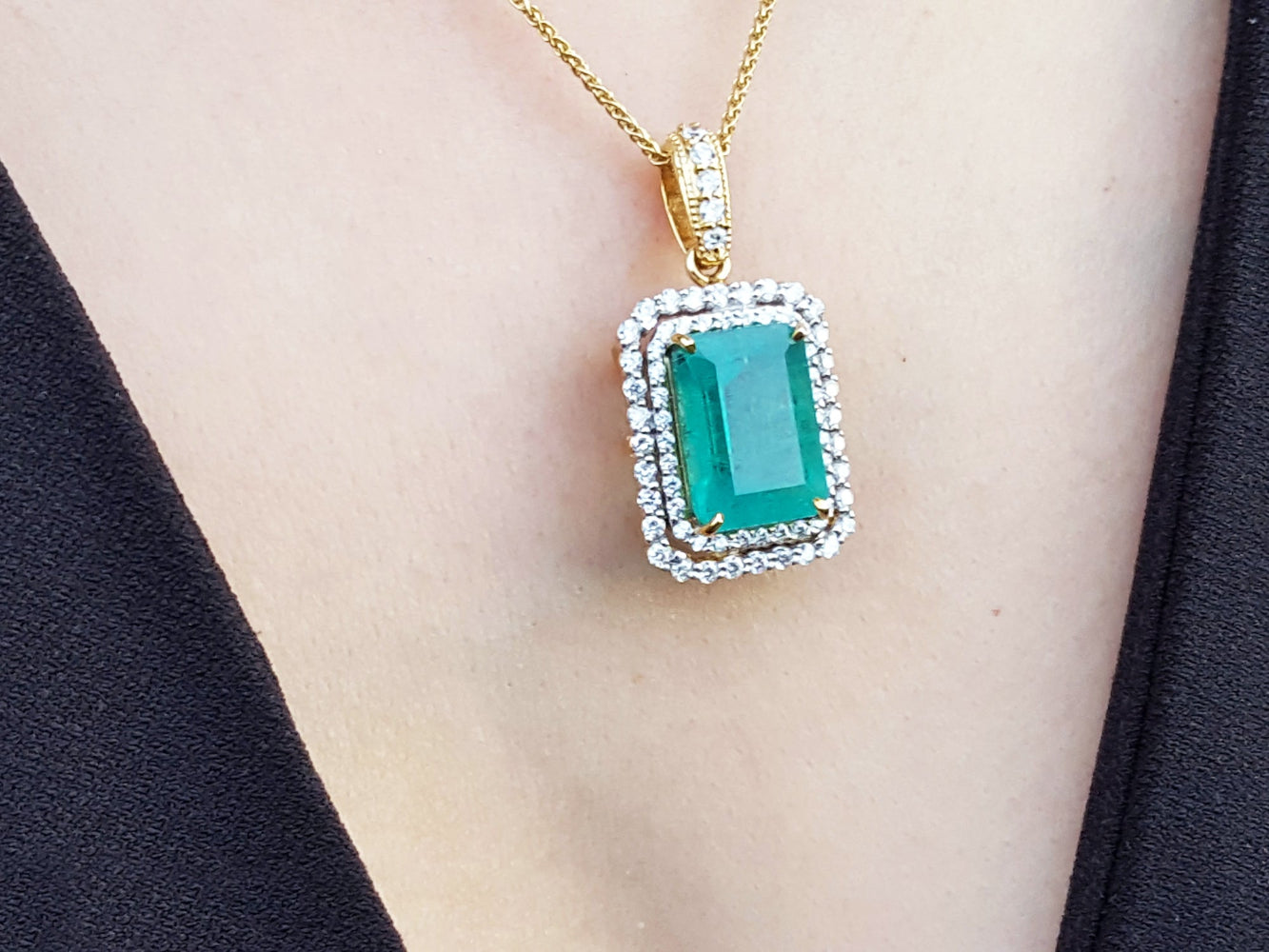 Gold necklace with a natural emerald into a double halo diamond pendant on a person's neck.