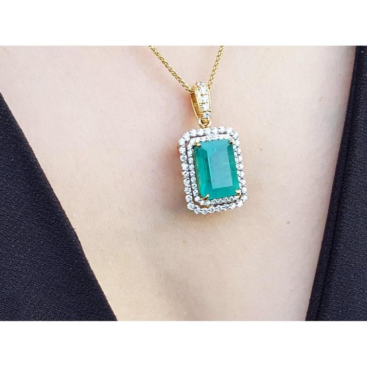 Gold necklace with a natural emerald into a double halo diamond pendant on a person's neck.