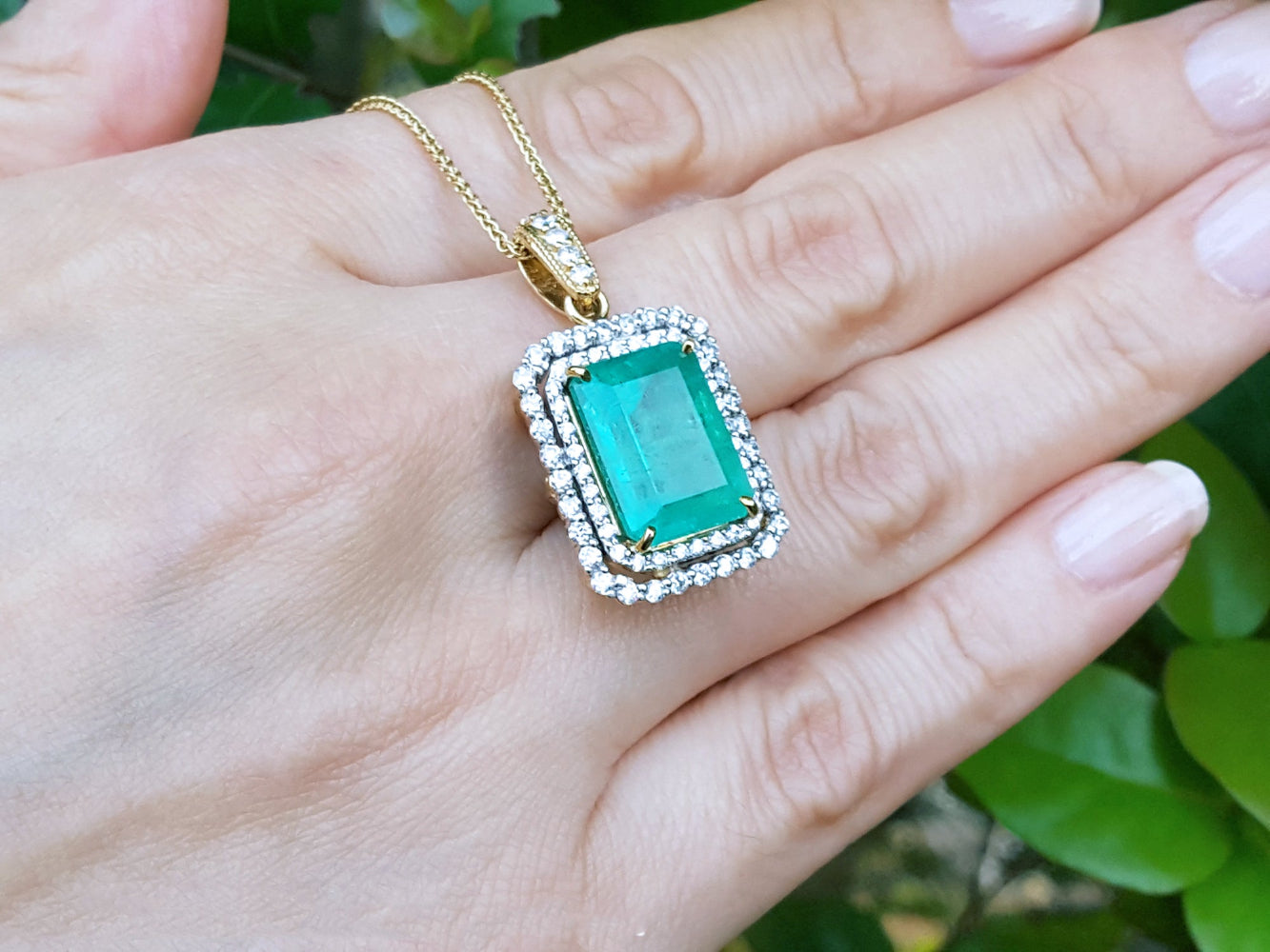 Gold necklace with a colombian emerald pendant held in a hand against a blurred green background