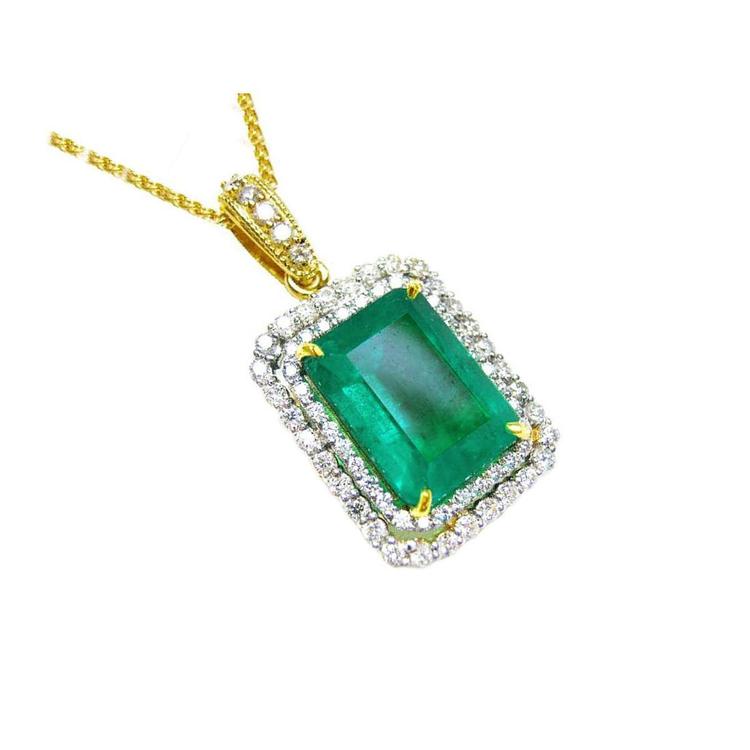 A yellow gold emerald pendant displaying the topside rectangular emerald surrounded by a double halo diamond.