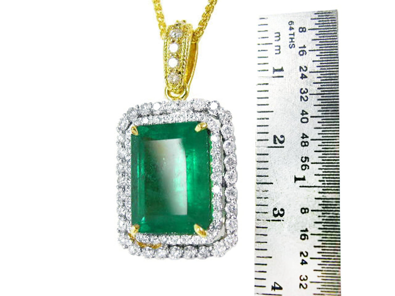 This yellow gold emerald pendant is next to a ruler for scale on a white background