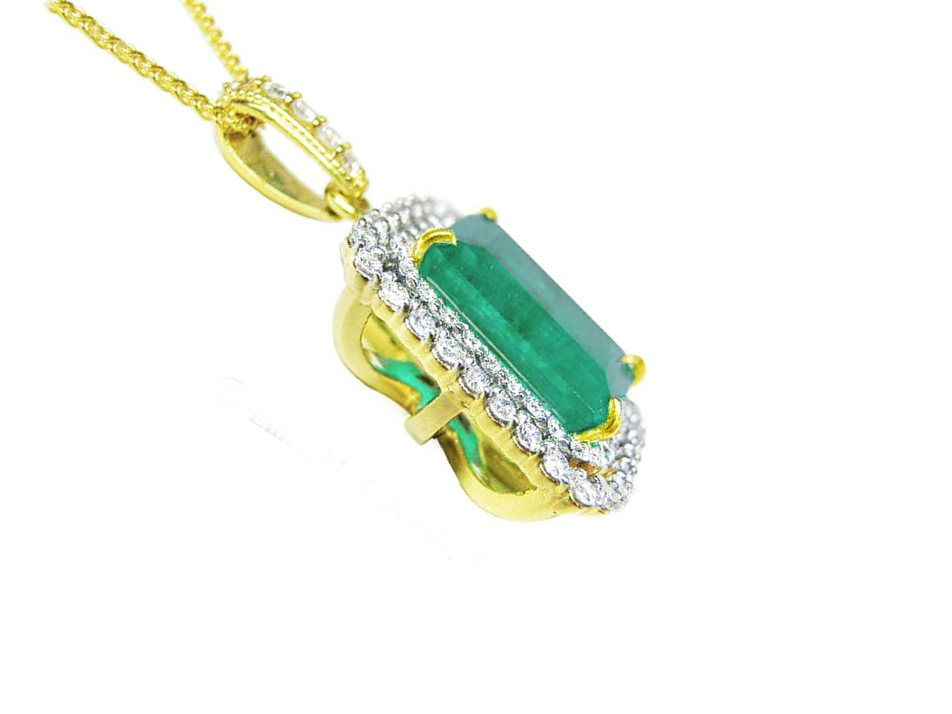 The underside profile view of a yellow gold pendant with a natural emerald and diamonds on a white background