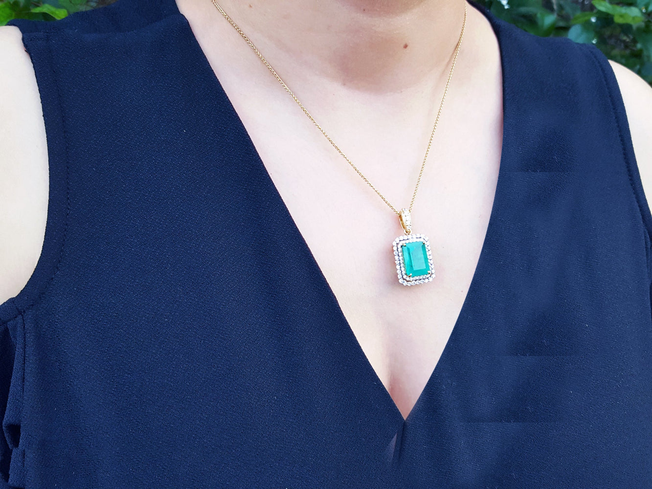 Person wearing a black sleeveless top with a gold necklace featuring an emerald pendant.