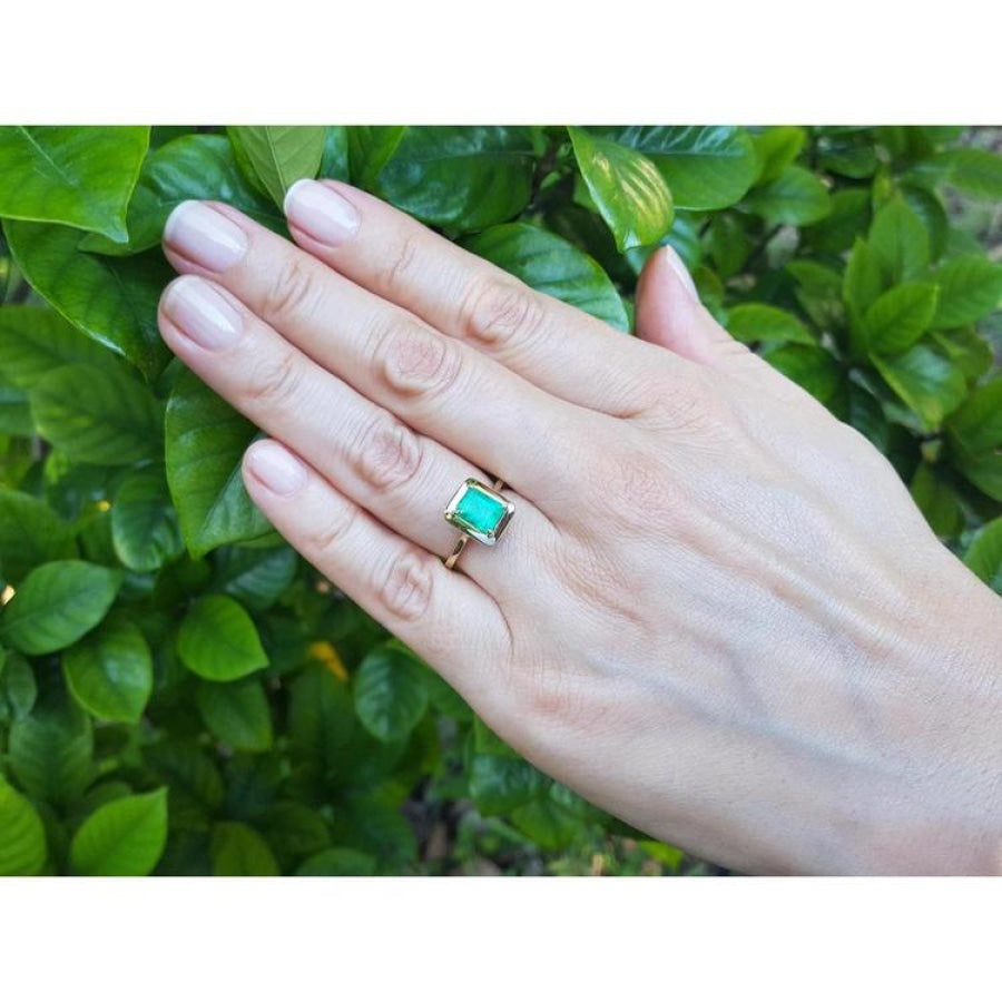 Hand wearing a 1.22 carat emerald-cut Muzo Colombian emerald solitaire ring in 14K yellow gold.