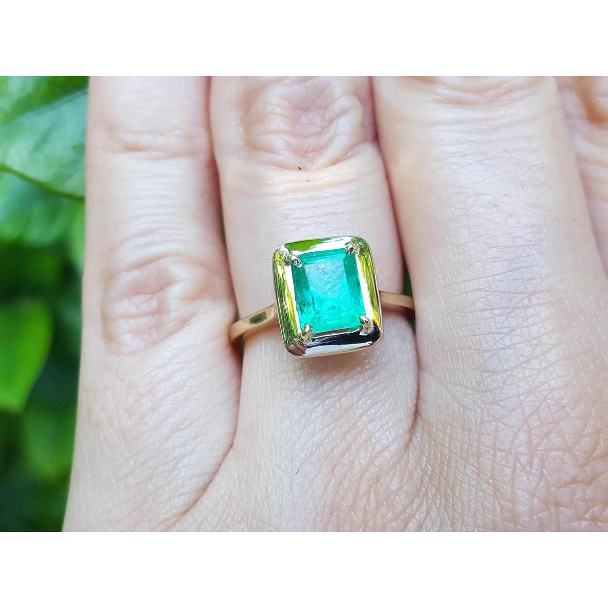 A yellow gold emerald solitaire ring on a person's finger.
