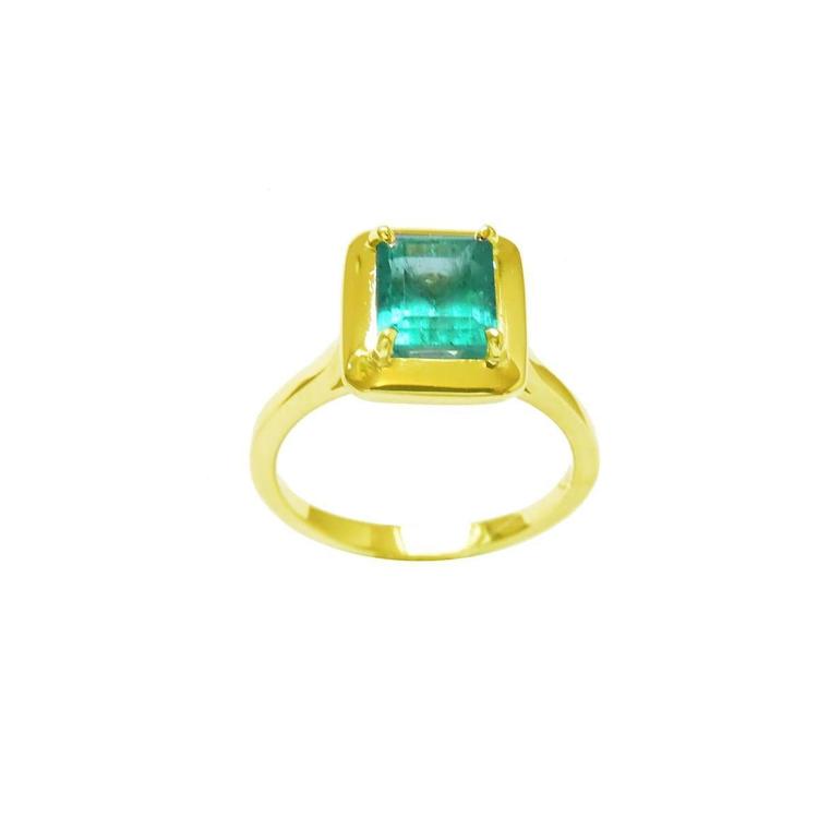A yellow gold emerald solitaire ring displaying a rectangular emerald into a wide bezel and prong set.