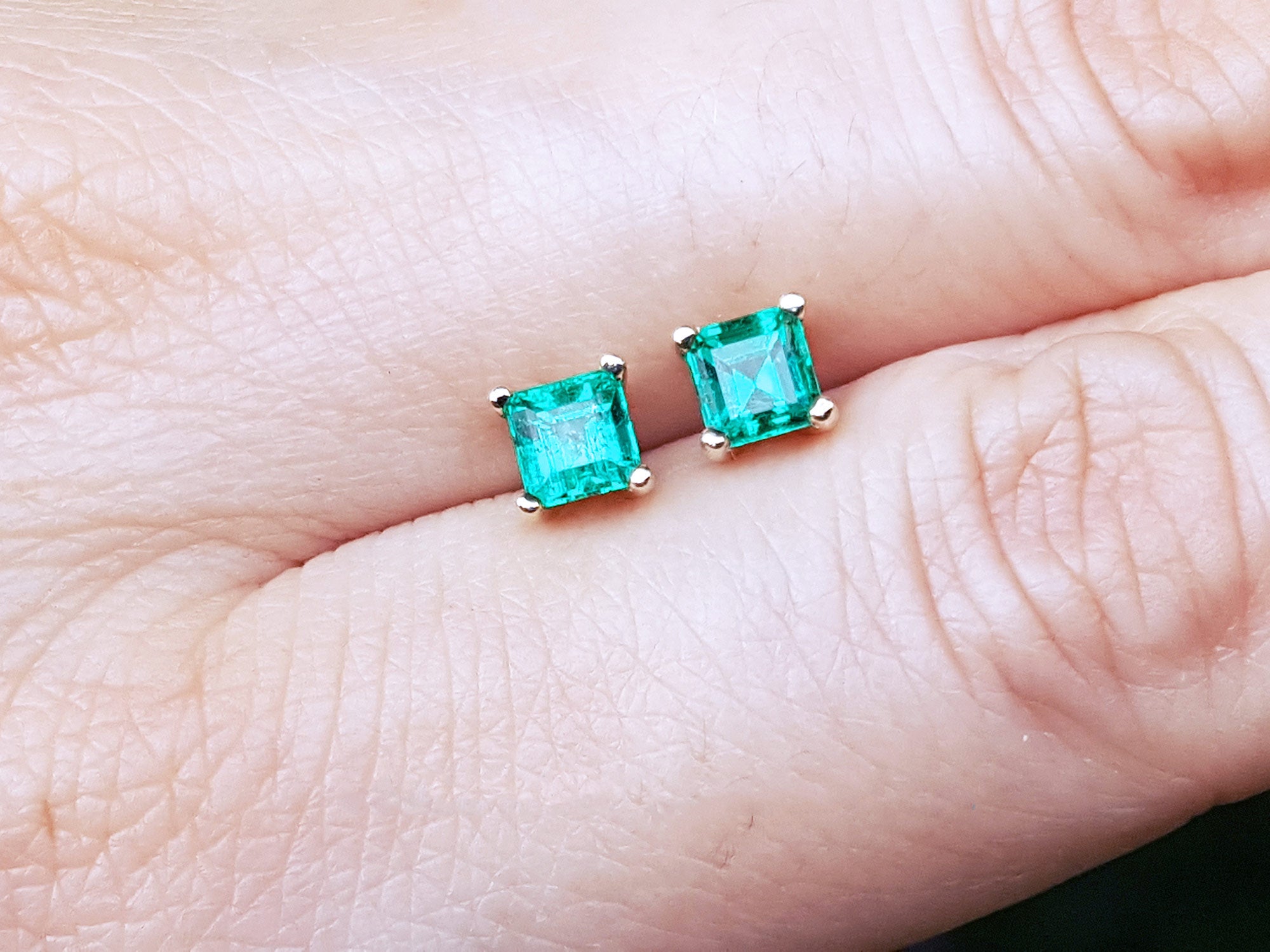 Natural emerald stud earrings on a person&#39;s finger